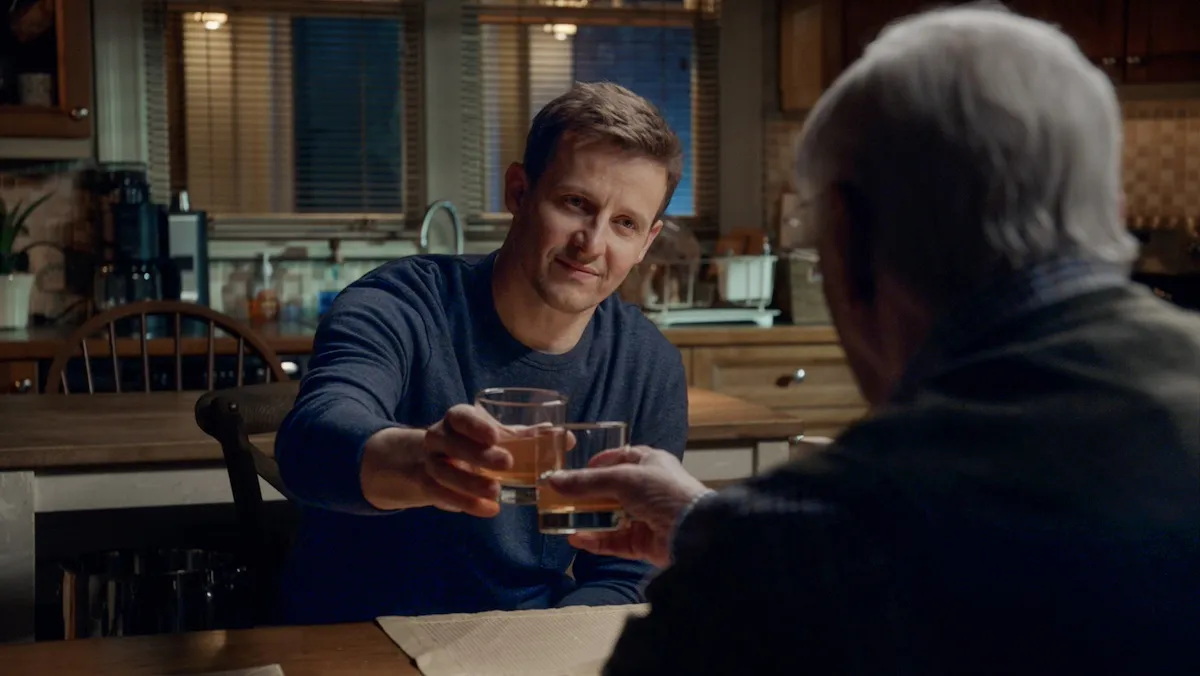 Jamie Reagan (Will Estes) sitting at a table and toasting with a glass