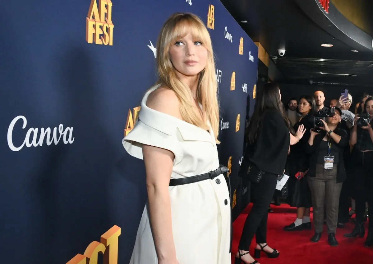 Wearing a white coat dress, Jennifer Lawrences stands on the red carpet with a visible baby bump while promoting "Zurawski v Texas"