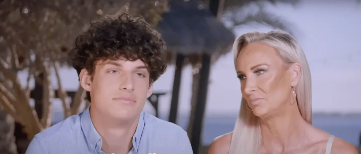 Young man with curly hair a blue button-down shirt next to an older woman with blonde hair