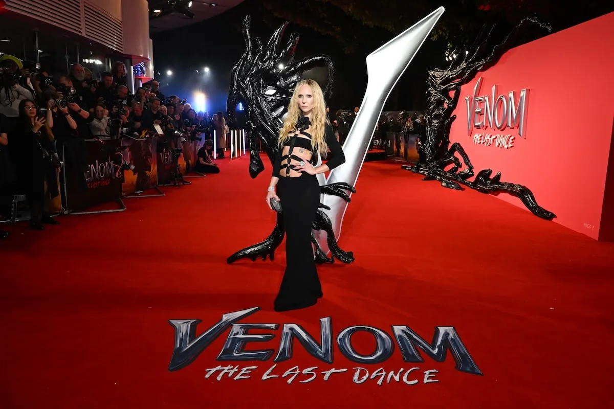 Wearing a black strappy dress, Juno Temple stands next to the Venom: The Last Dance logo