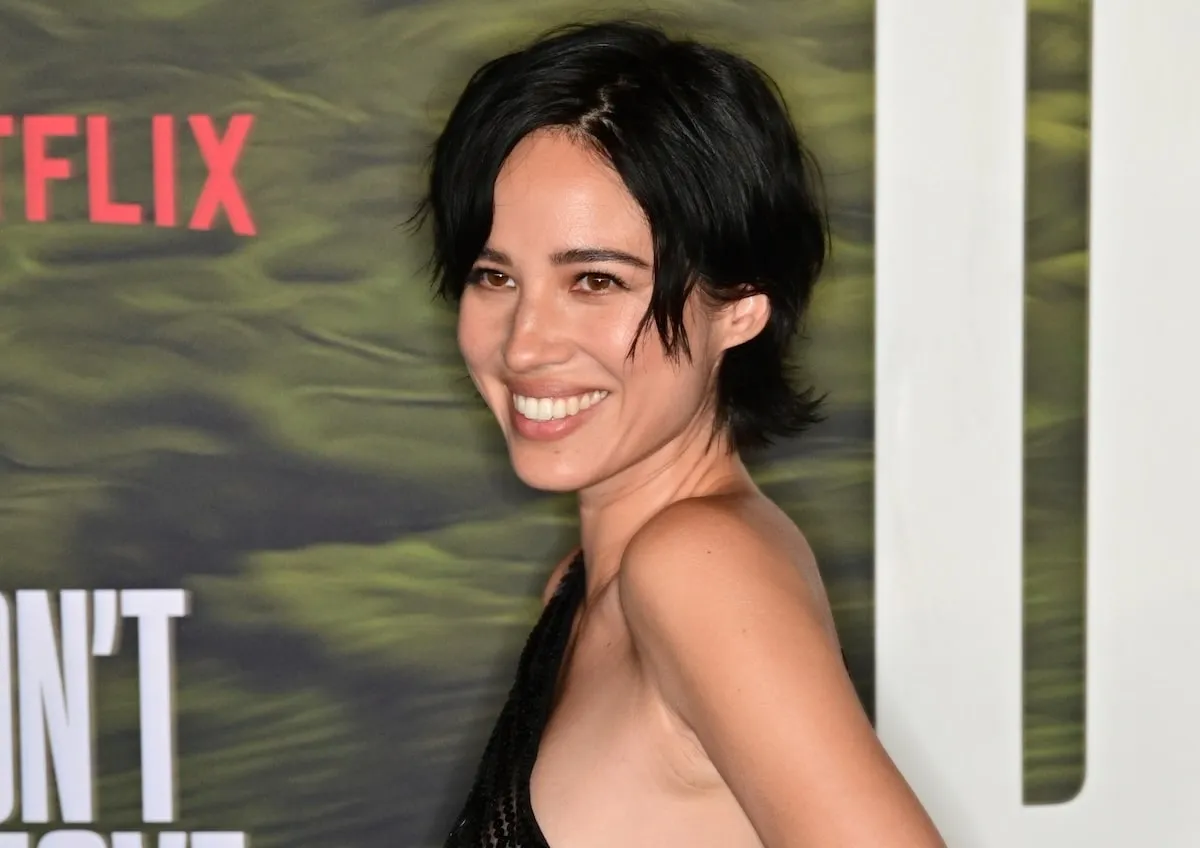 Wearing a black sheer dress, Kelsey Asbille smiles for cameras on the red carpet of the Don't Move photo call