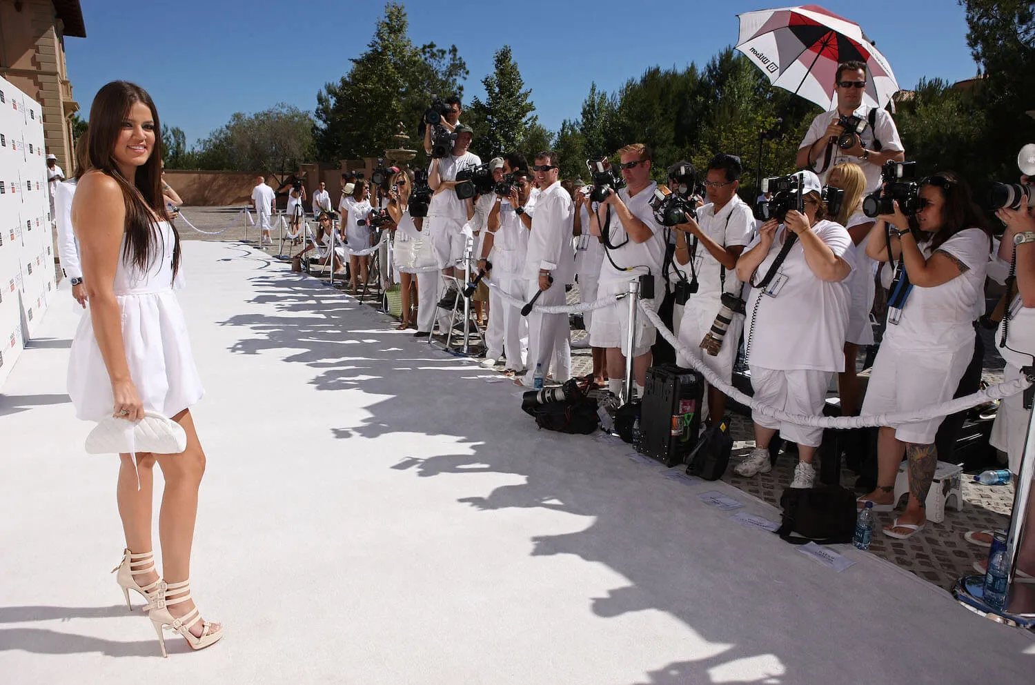 Khloé Kardashian in a white dress posing in front of photographers dressed in white at a  Sean 'Diddy' Combs White Party.