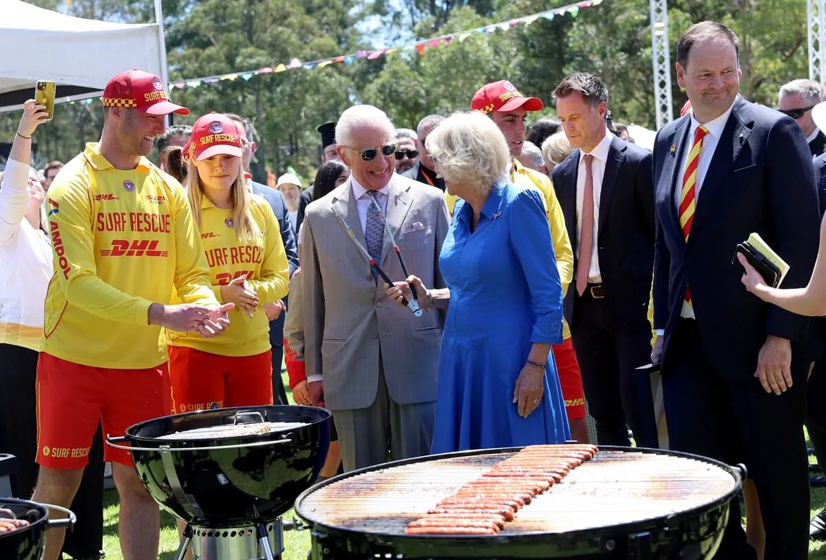 King Charles III and Queen Camilla cook sausages for the food stalls at the Premier's Community Barbeque at Parramatta Park in Sydney, Australia