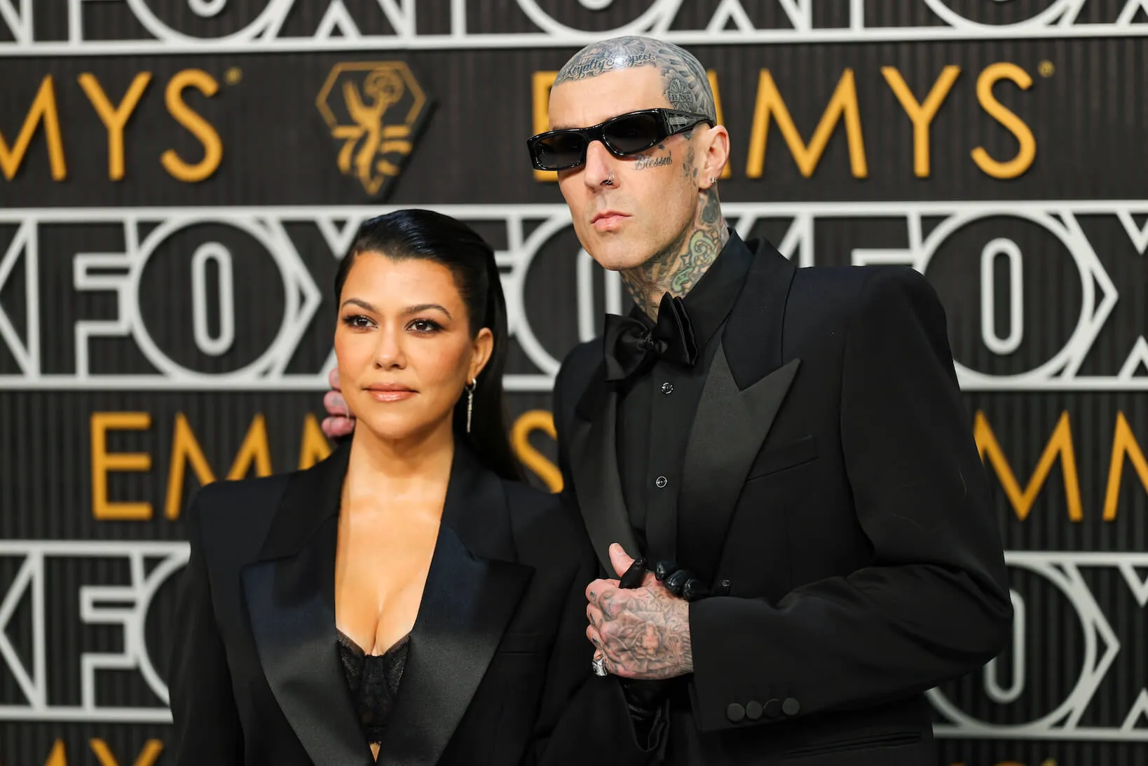 Kourtney Kardashian and Travis Barker side by side at the Emmy Awards. Both are wearing black dresses.