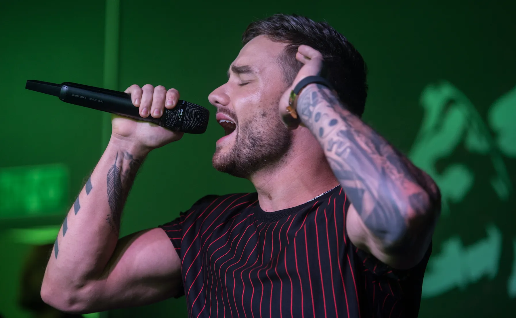 Liam Payne singing soulfully into a microphone with his eyes closed and one hand up by his ear.