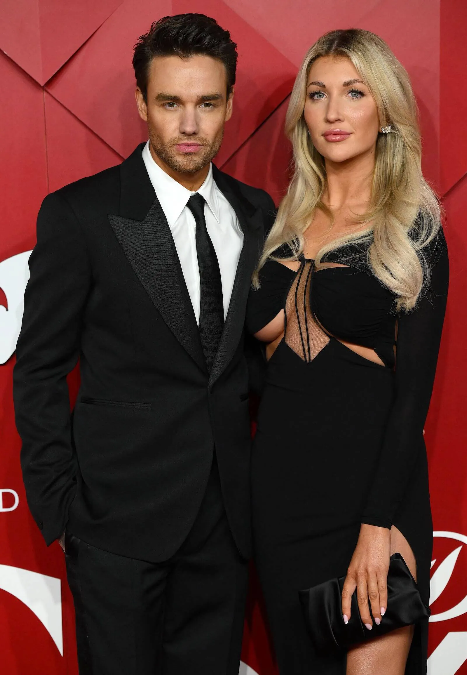 Liam Payne in a black suit and Kate Cassidy in a black dress posing together at an event.