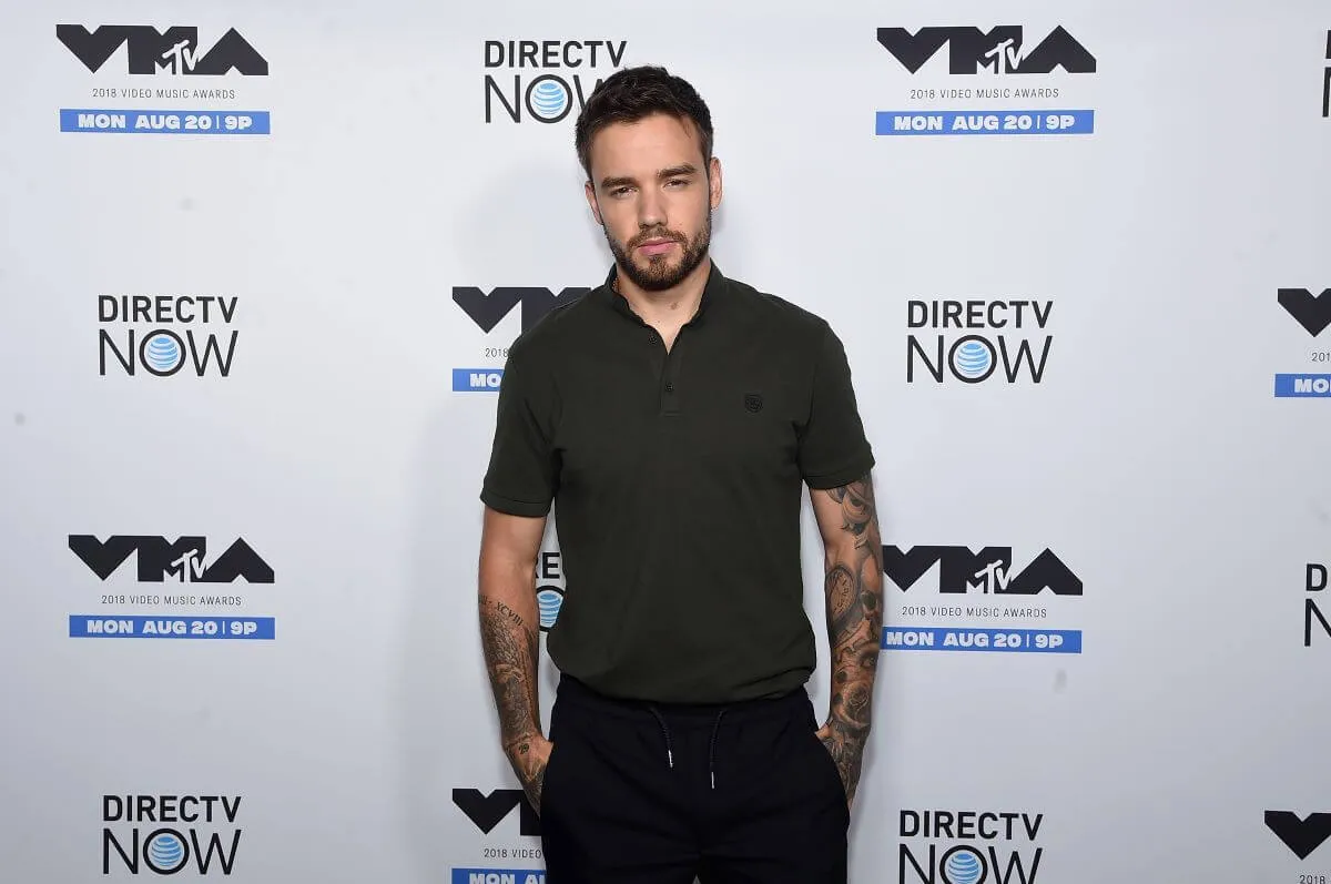 Liam Payne wears a black collared shirt and stands with his hands in his pockets.