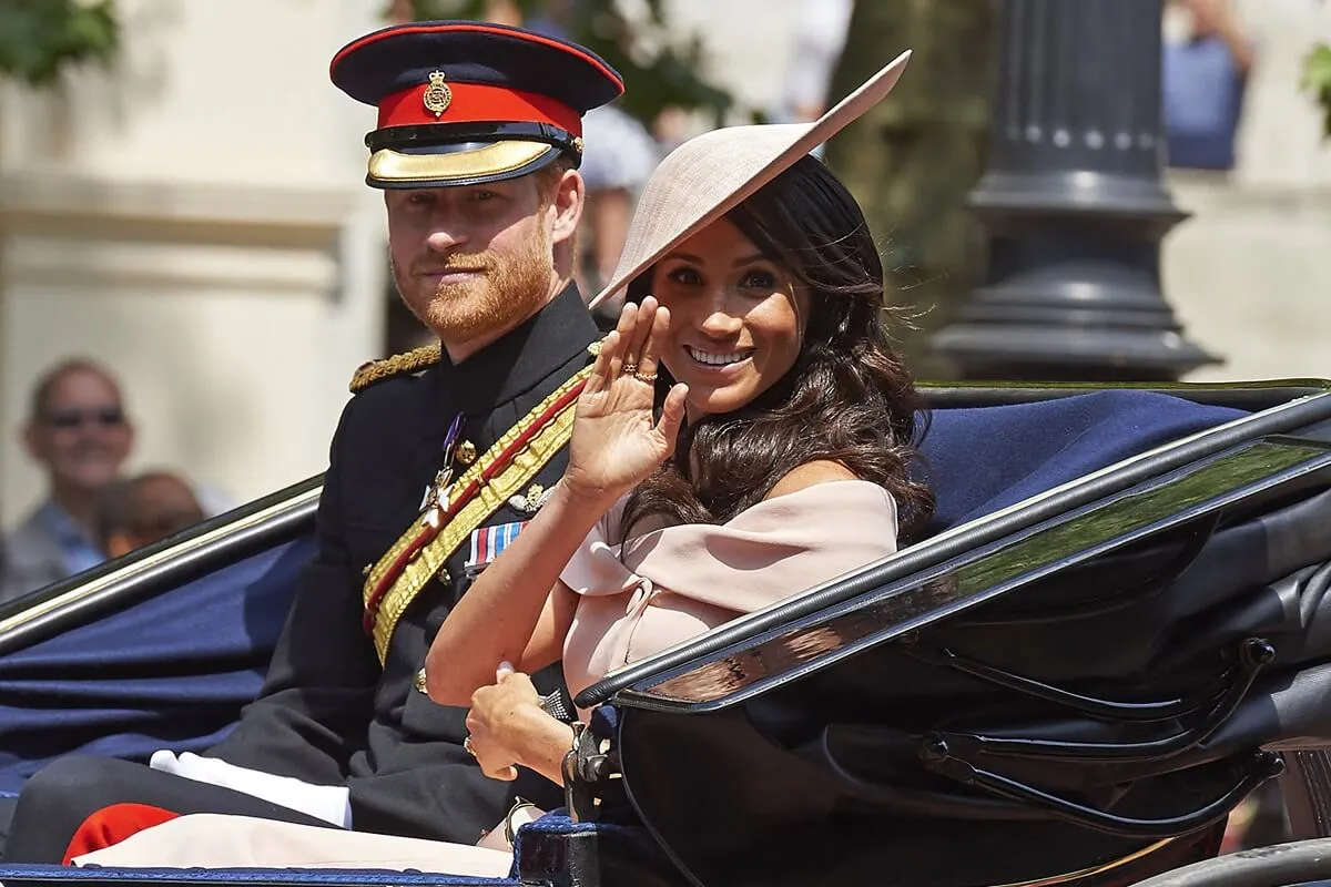 Meghan Markle waves as she and Prince Harry ride in a horse-drawn carriage after attending the 2018 Trooping the Colour