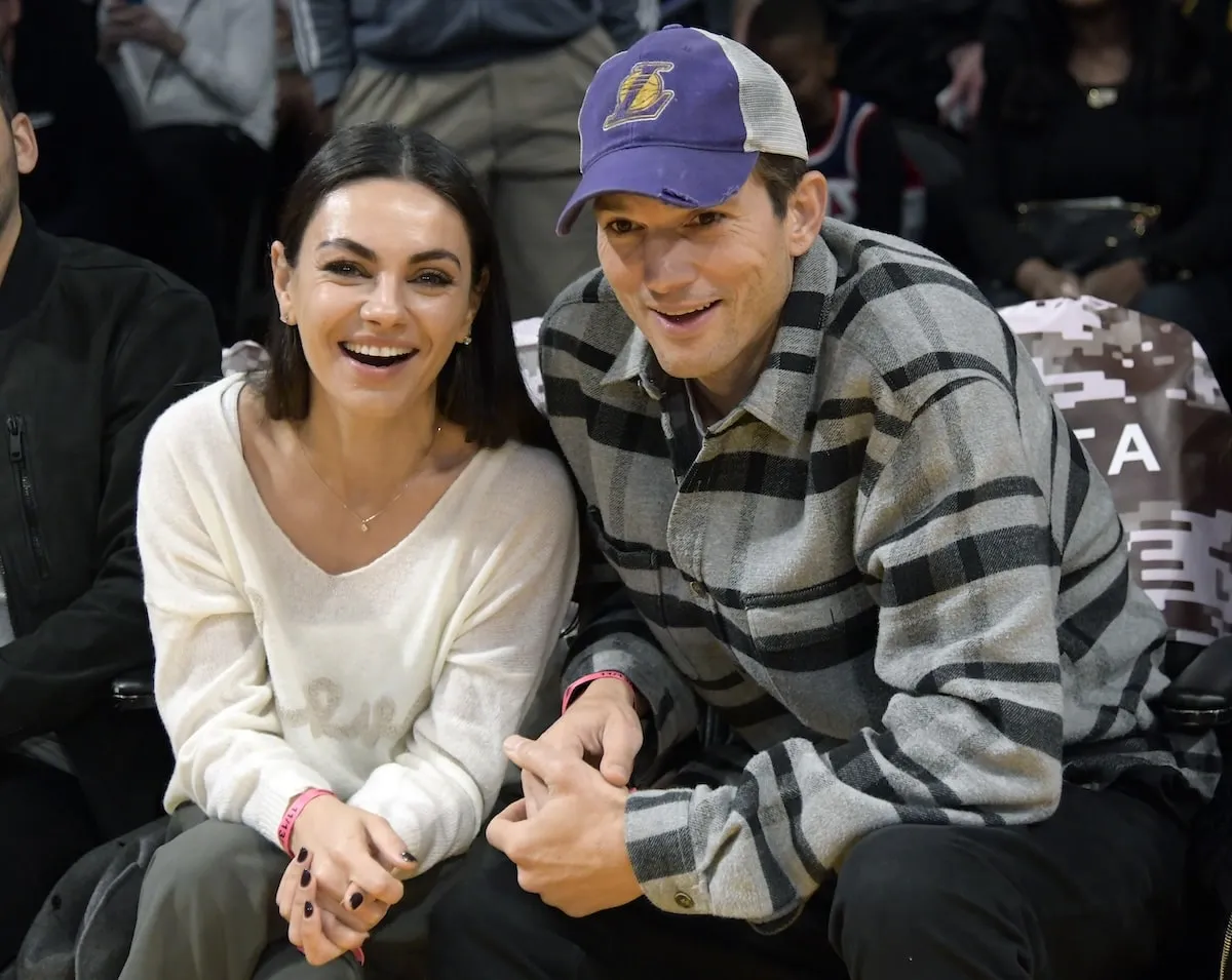 Actors Mila Kunis and Ashton Kutcher laugh together at a Lakers game in 2022