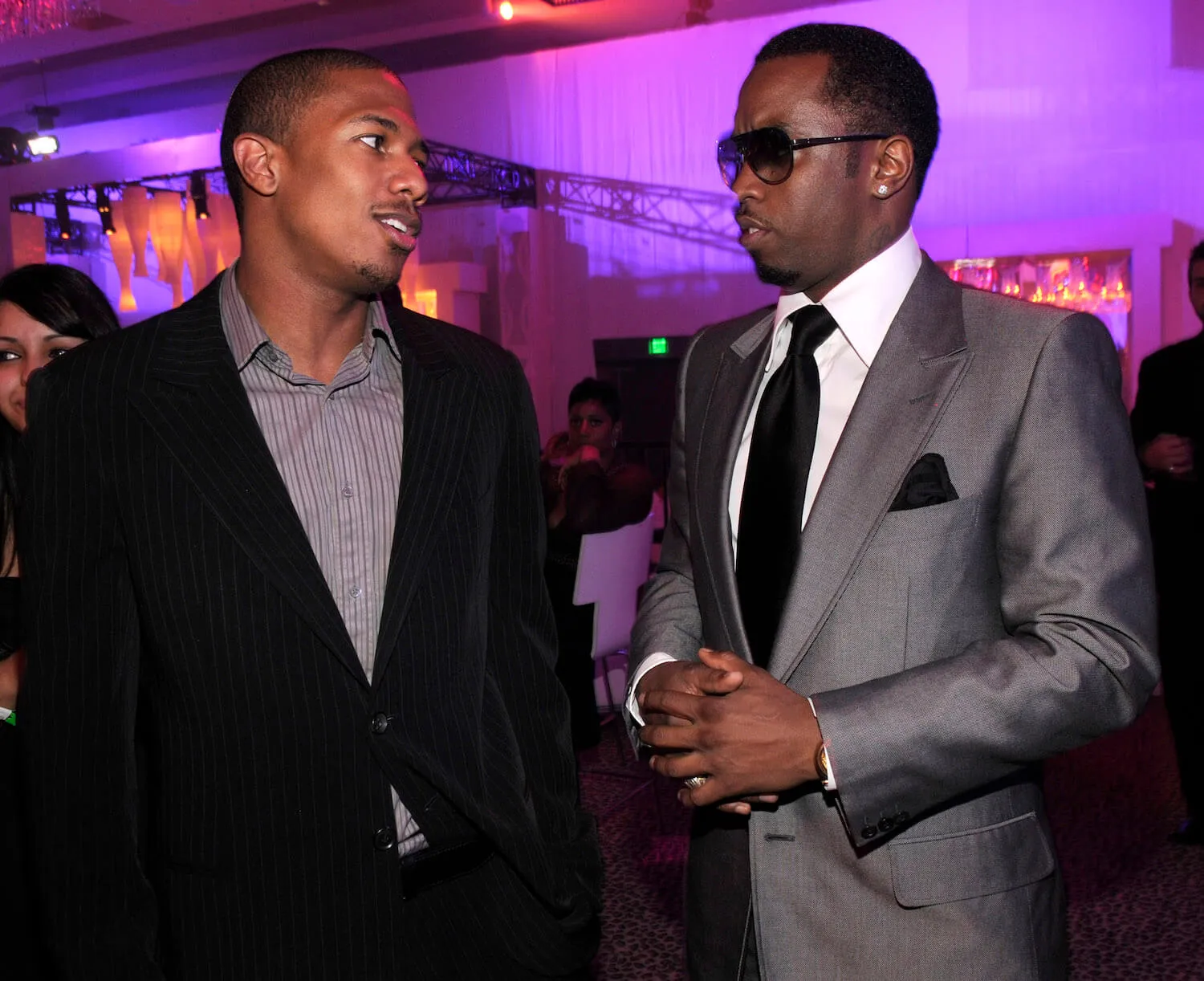 Nick Cannon and Sean 'Diddy' Combs looking at each other and talking at a party in 2008. They are against a purple background and wearing suits.