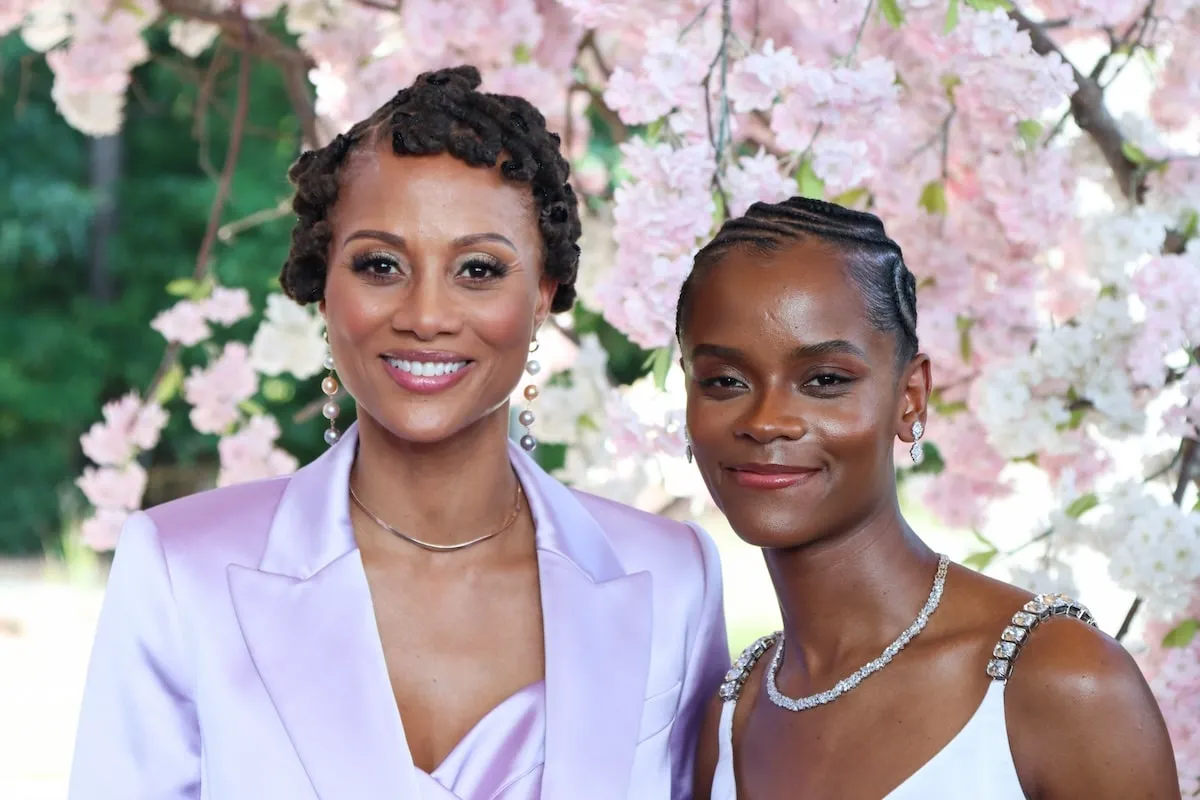 Co-stars of Possum Trot, Nika King and Letitia Wright, wear lavender and white and stand beneath a pink flowering tree