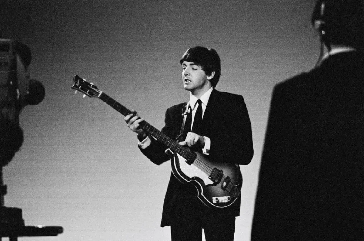 A black and white picture of Paul McCartney wearing a suit and holding a guitar.