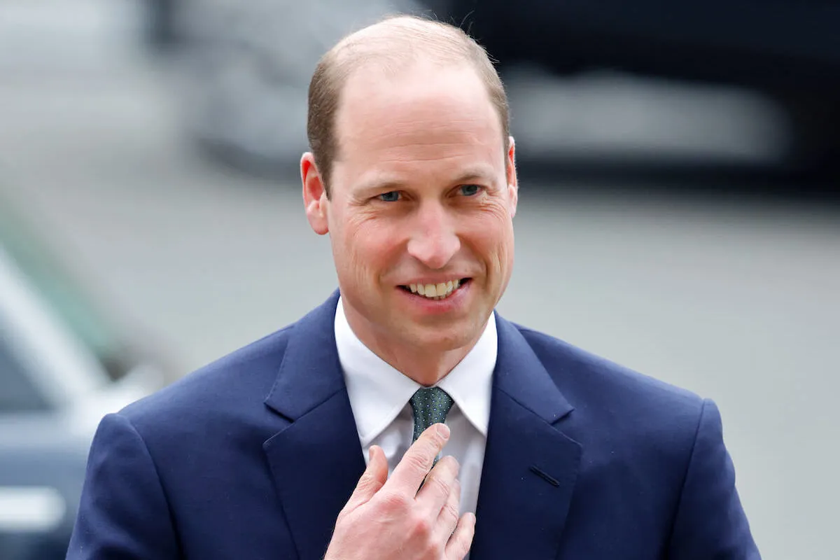 Prince William smiles and adjusts his tie.