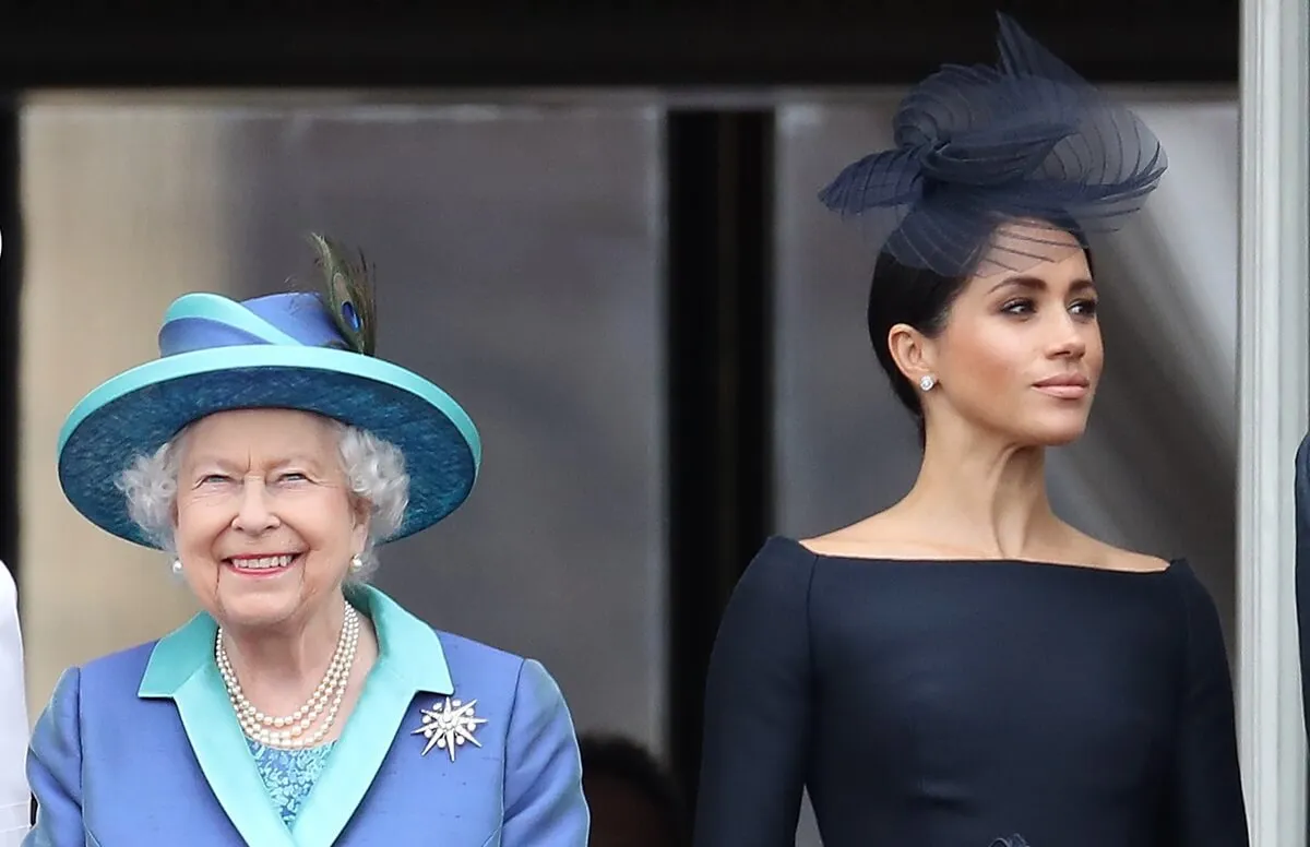 Queen Elizabeth II and Meghan Markle standing on the balcony of Buckingham Palace during a flyover