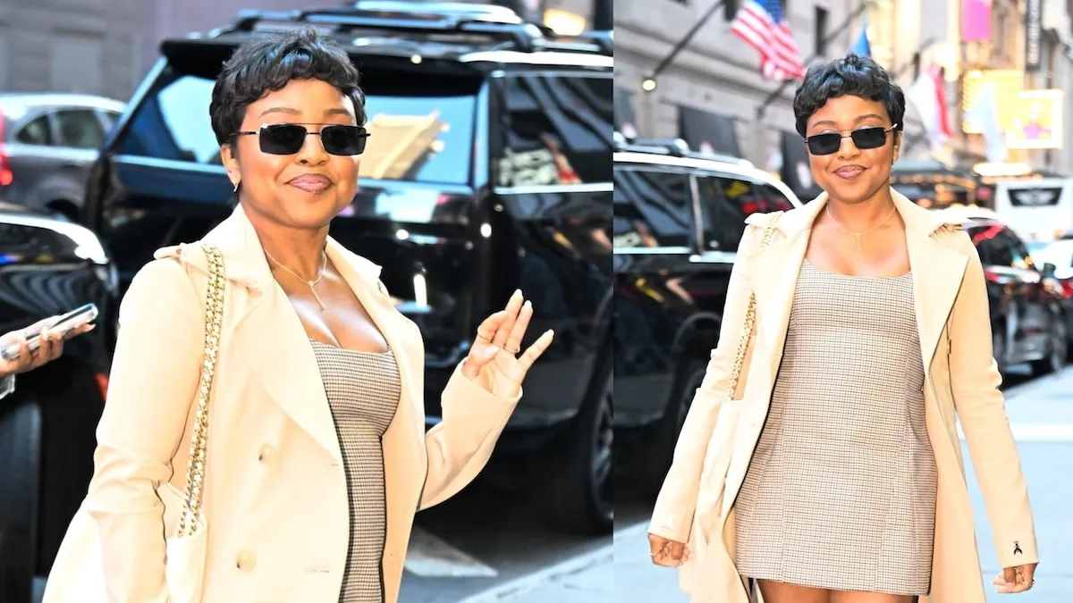 Wearing a beige trench coat and plaid mini dress, Quinta Brunson waves to cameras outside of ABC Studios