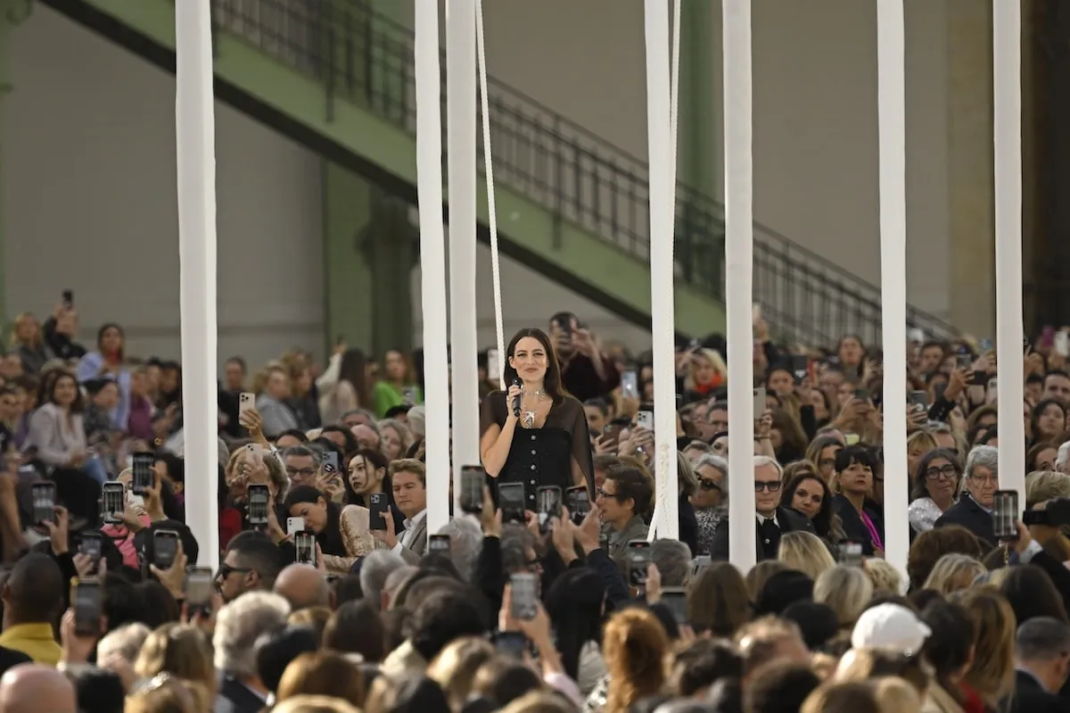 Wearing a black dress and cape, Riley Keough performs on the runway during the Chanel Paris Womenswear Spring-Summer 2025 show