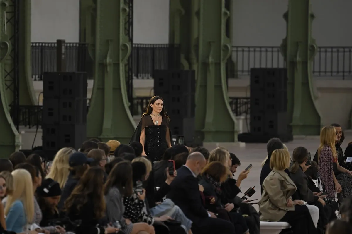 Wearing a black dress and cape, Riley Keough performs on the runway during the Chanel Paris Womenswear Spring-Summer 2025 show