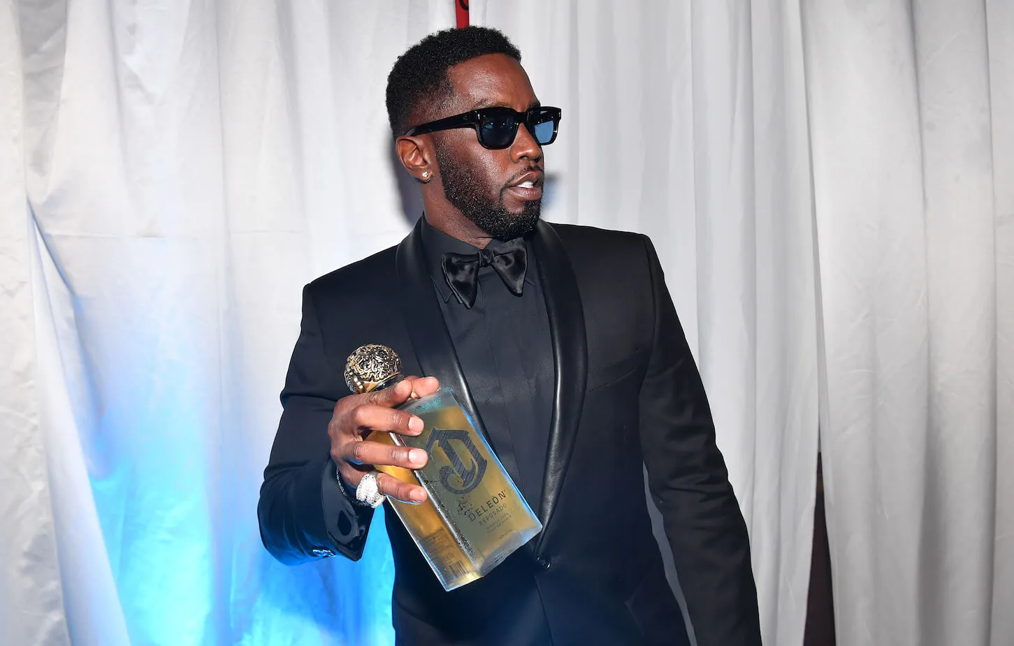 Sean 'Diddy' Combs dressed in a black suit holding a bottle of liquor in 2022.