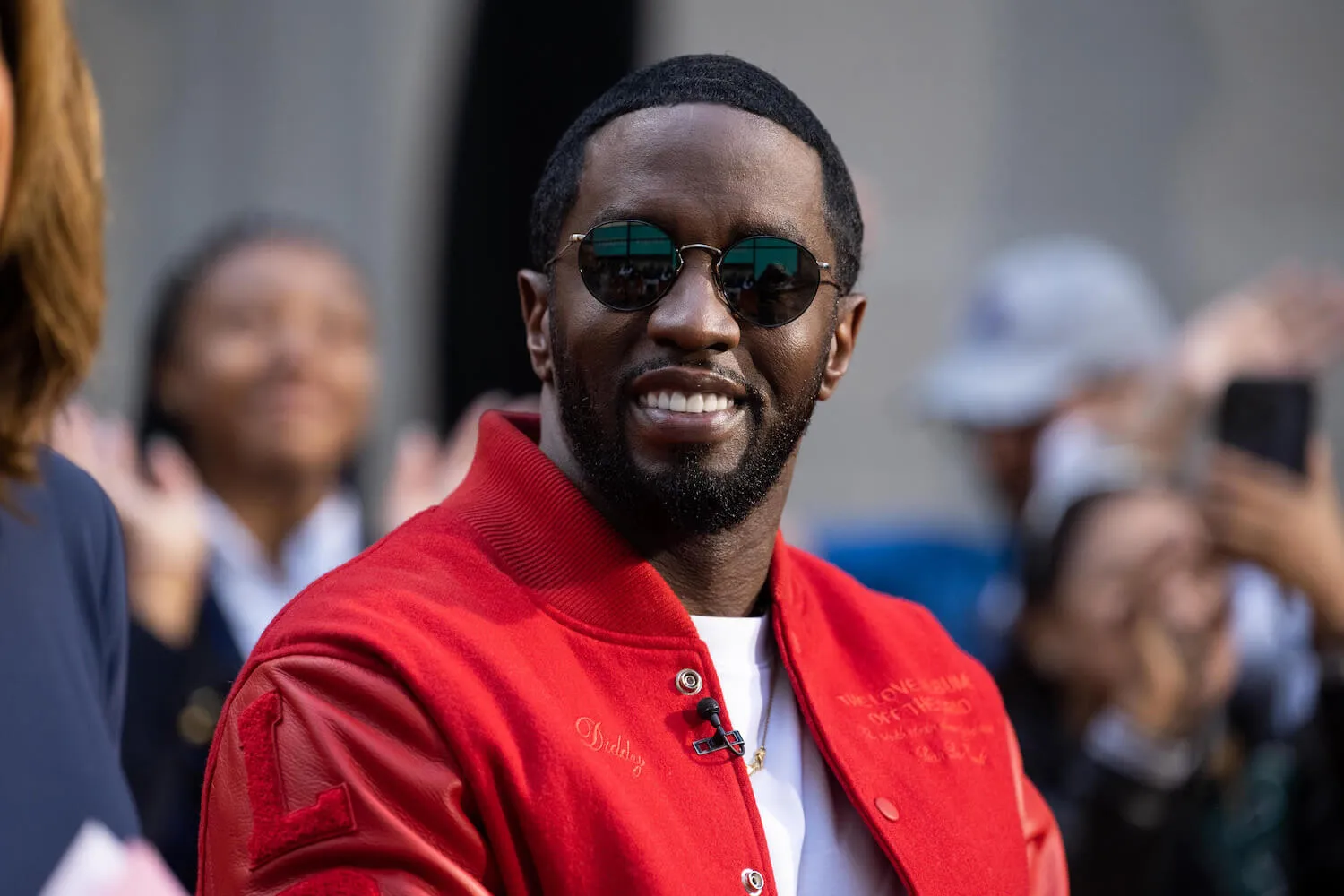 Sean 'Diddy' Combs smiling in a red jacket with sunglasses on.