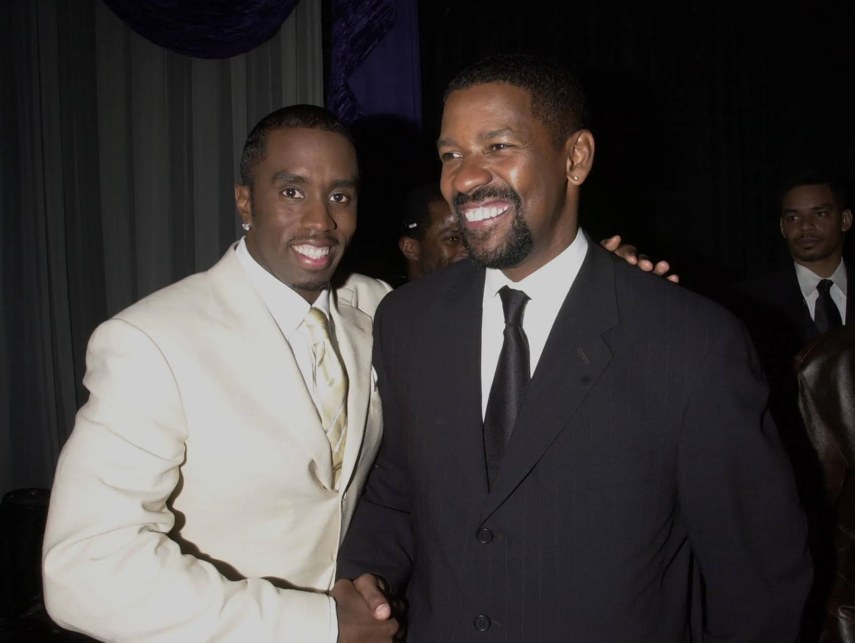 Sean 'Diddy' Combs in a white suit and Denzel Washington in a black suit smiling at an event in 2001