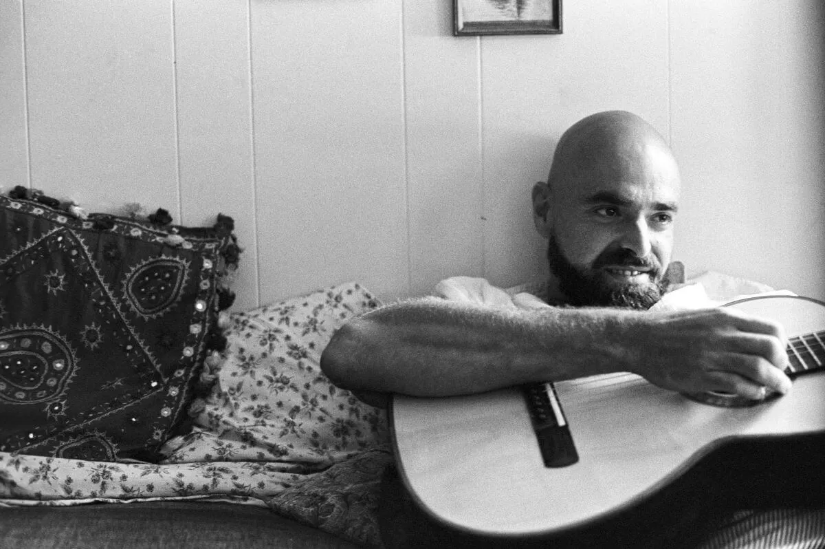 A black and white picture of Shel Silverstein sitting and  holding a guitar.