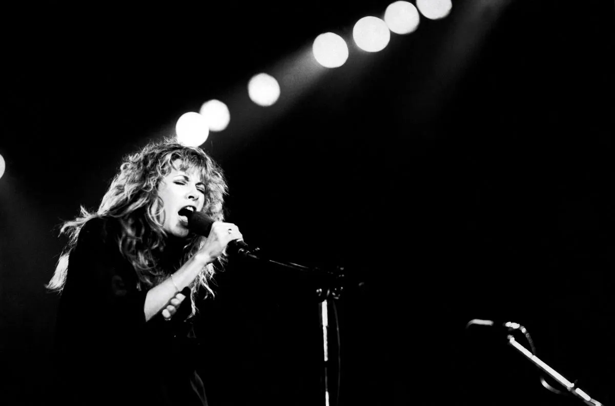 A black and white picture of Stevie Nicks singing into a microphone while on stage.