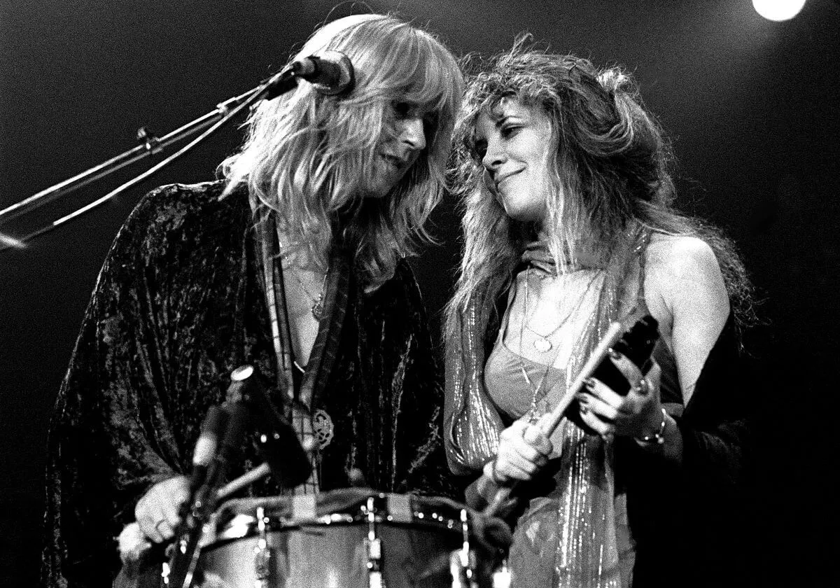 A black and white picture of Christine McVie and Stevie Nicks standing onstage together.