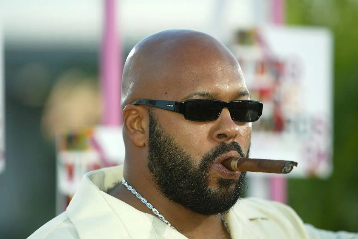 Suge Knight wears sunglasses and holds a cigar in his mouth.