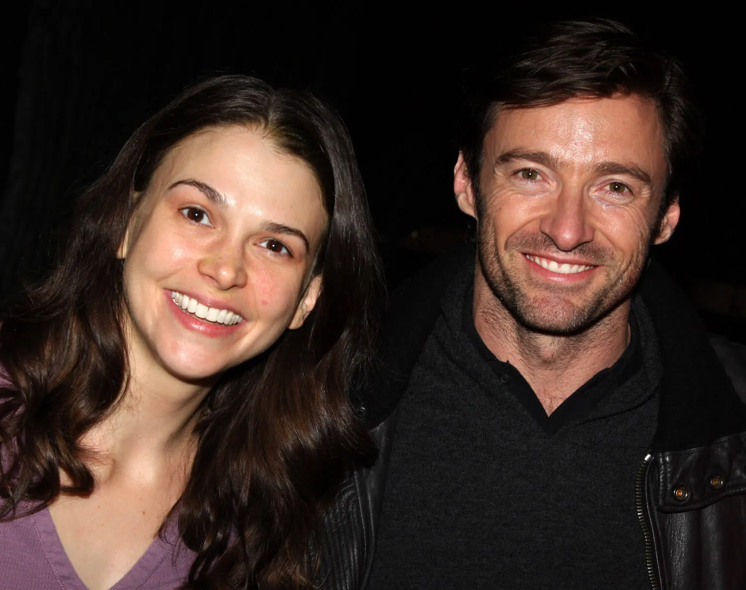 Sutton Foster and Hugh Jackman smiling together in 2008 against a dark background.