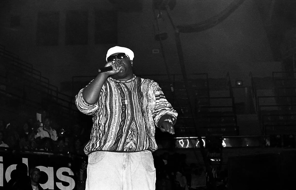 A black and white picture of The Notorious B.I.G. wearing a sweater and hat while performing.