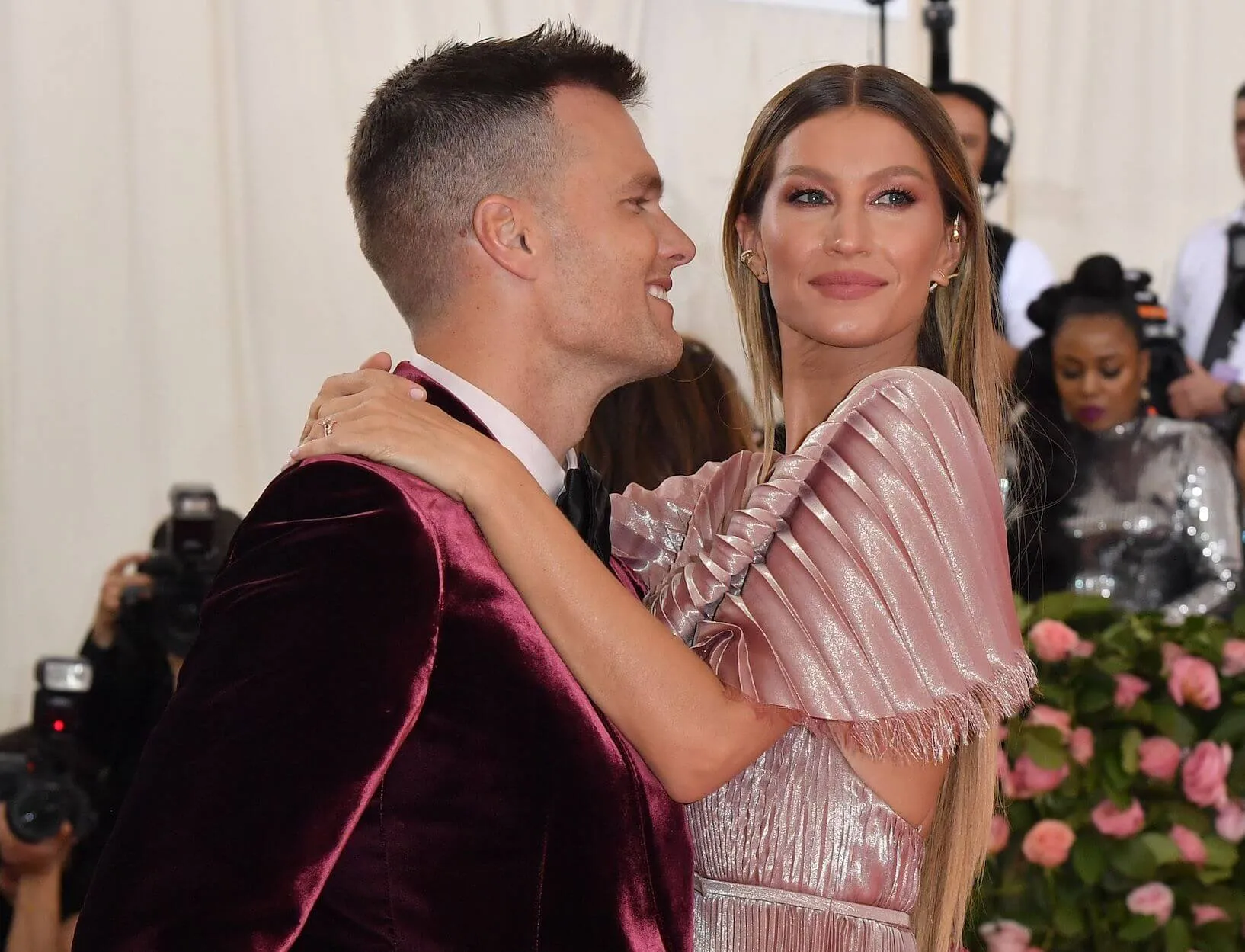 Tom Brady gazing lovingly at Gisele Bundchen as she puts her arms around his neck and looks forward at the Met Gala in 2019