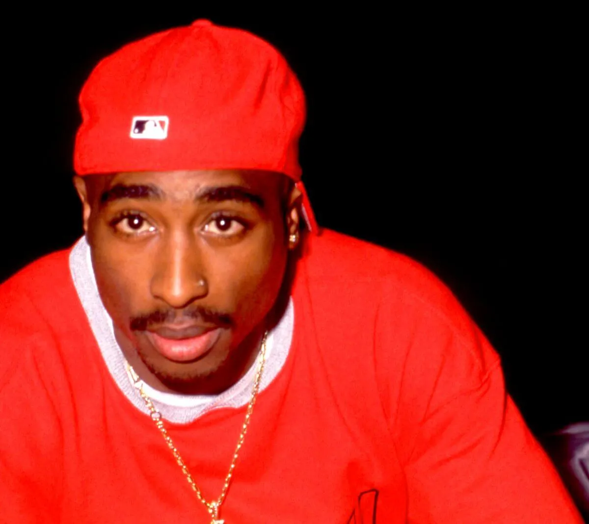 Tupac Shakur wears a red hat and a red shirt.