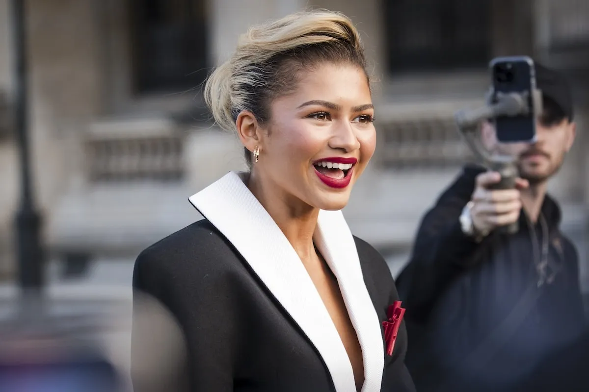 Wearing a black blazer and beige bubble skirt, Zendaya smiles for cameras and walks across the plaza before the Louis Vuitton show