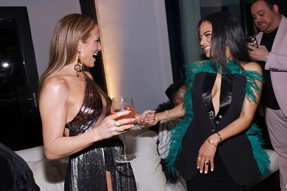 Jennifer Lopez and Christina Milian attend the launch of JLo Jennifer Lopez for Revolve Collection at a private residence wearing a brown and green dress respectively.