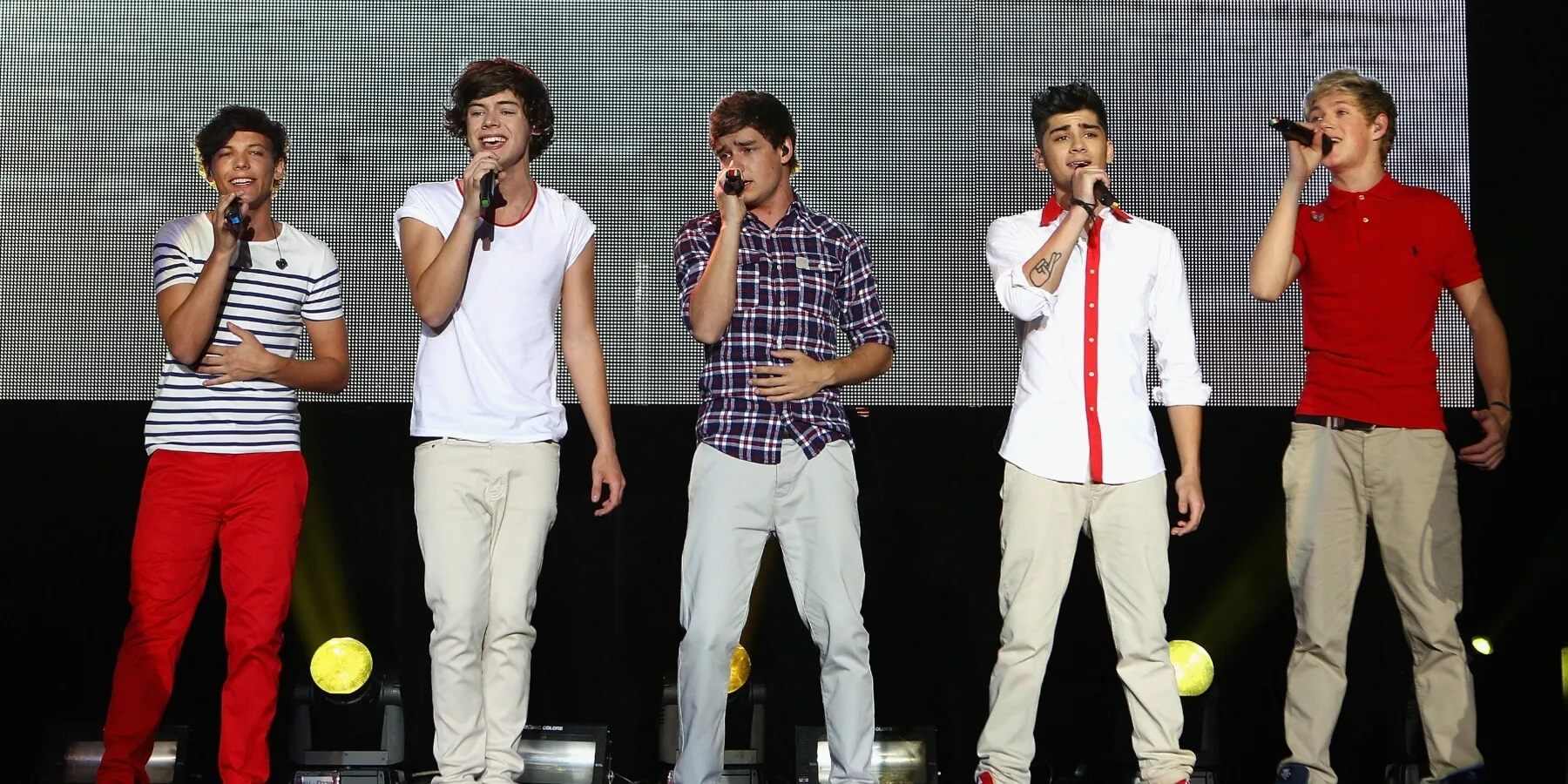 Louis Tomlinson, Harry Styles, Liam Payne, Zayn Malik, Niall Horan of One Direction sing into microphones.