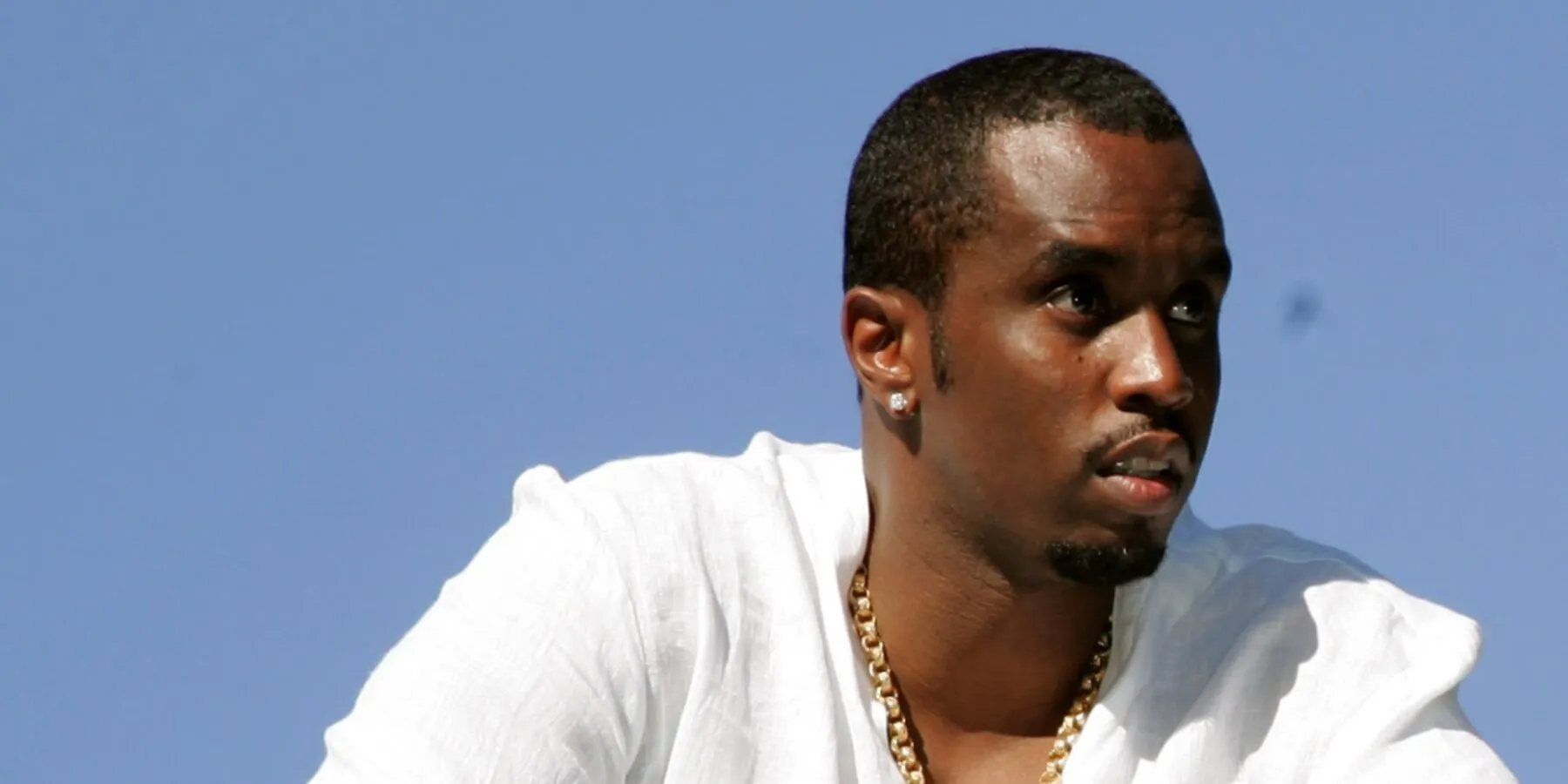 Sean 'Diddy Combs' wears a white shirt and poses in front of a blue background.