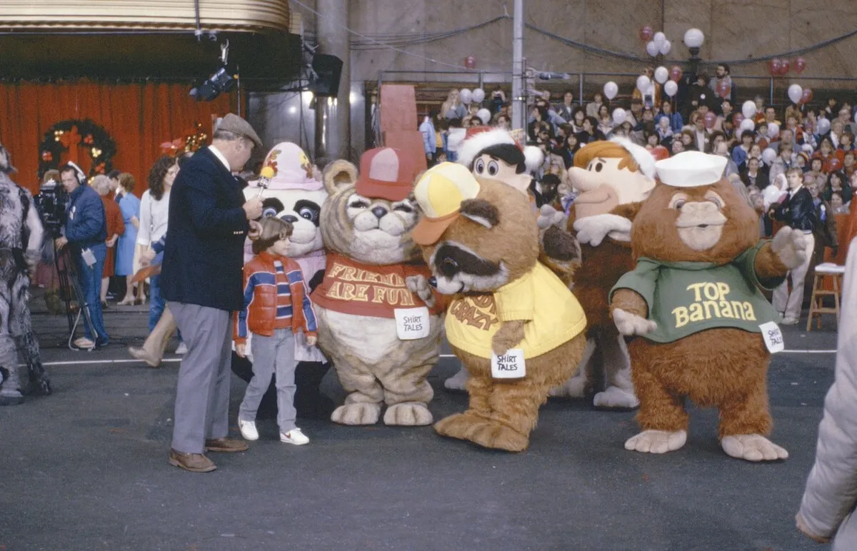 A man a bow talk to people dressed as characters from Shirt Tales at the Macy's parade in 1983