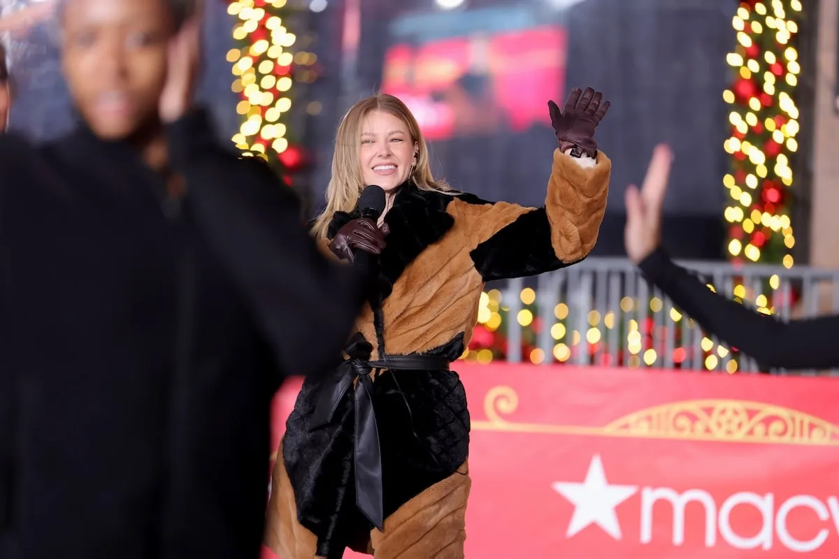 Wearing a black and brown coat and pants, Ariana Madix holds a microphone while rehearsing for the Macy's Thanksgiving Day Parade