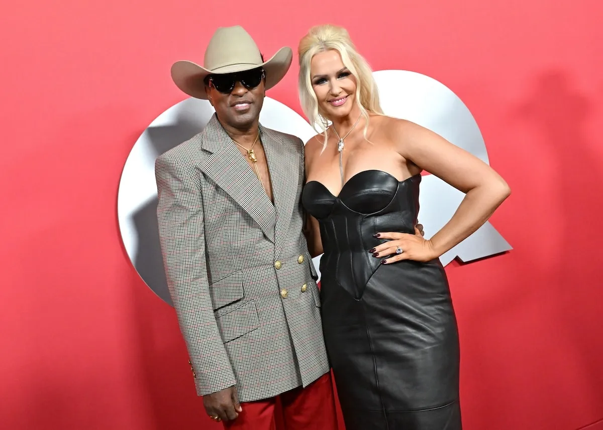 Wearing a checked jacket and cowboy hat, Kenny 'Babyface' Edmonds poses with Rika Tischendorf on the red carpet at the 2024 GQ Men Of The Year Party