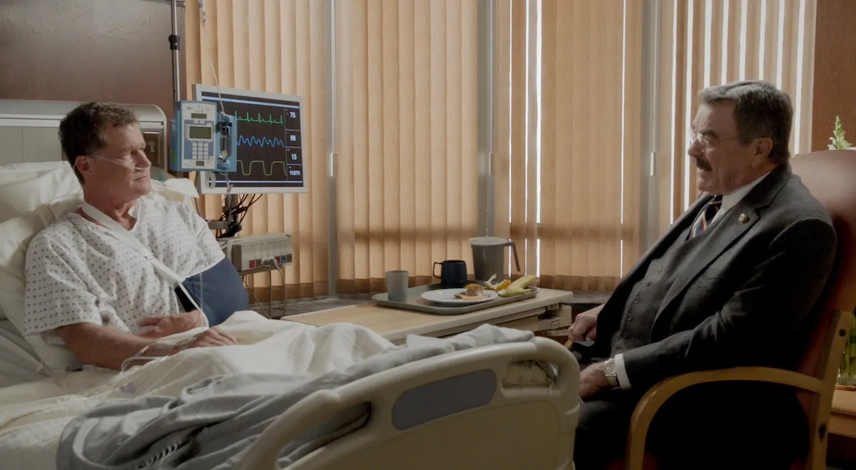 Tom Selleck talks to a man in a hospital bed with his arm in a sling in the 'Blue Bloods' Season 14 finale