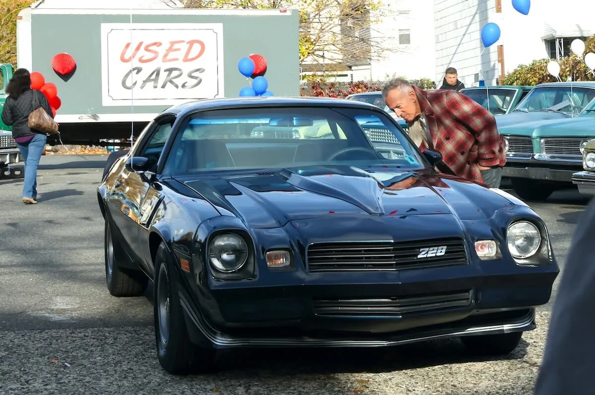 Bruce Springsteen looks into the window of black vintage muscle car