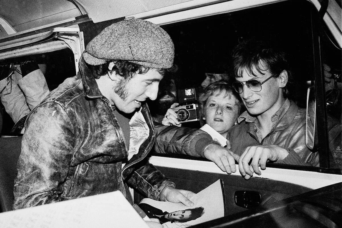 Black and white photo of Bruce Springsteen in a car signing an autograph for a fan