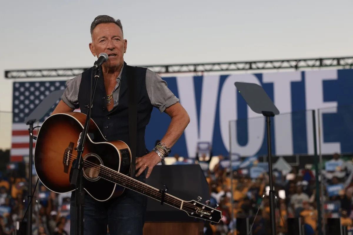 Bruce Springsteen holding a guitar in front of sign reading "vote"