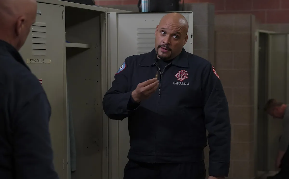 Cruz standing in front of his locker and holding a bullet pendant in 'Chicago Fire' Season 13