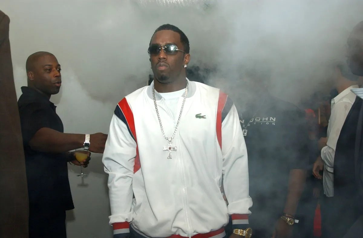 Diddy wears a white jacket and sunglasses and walks through smoke.