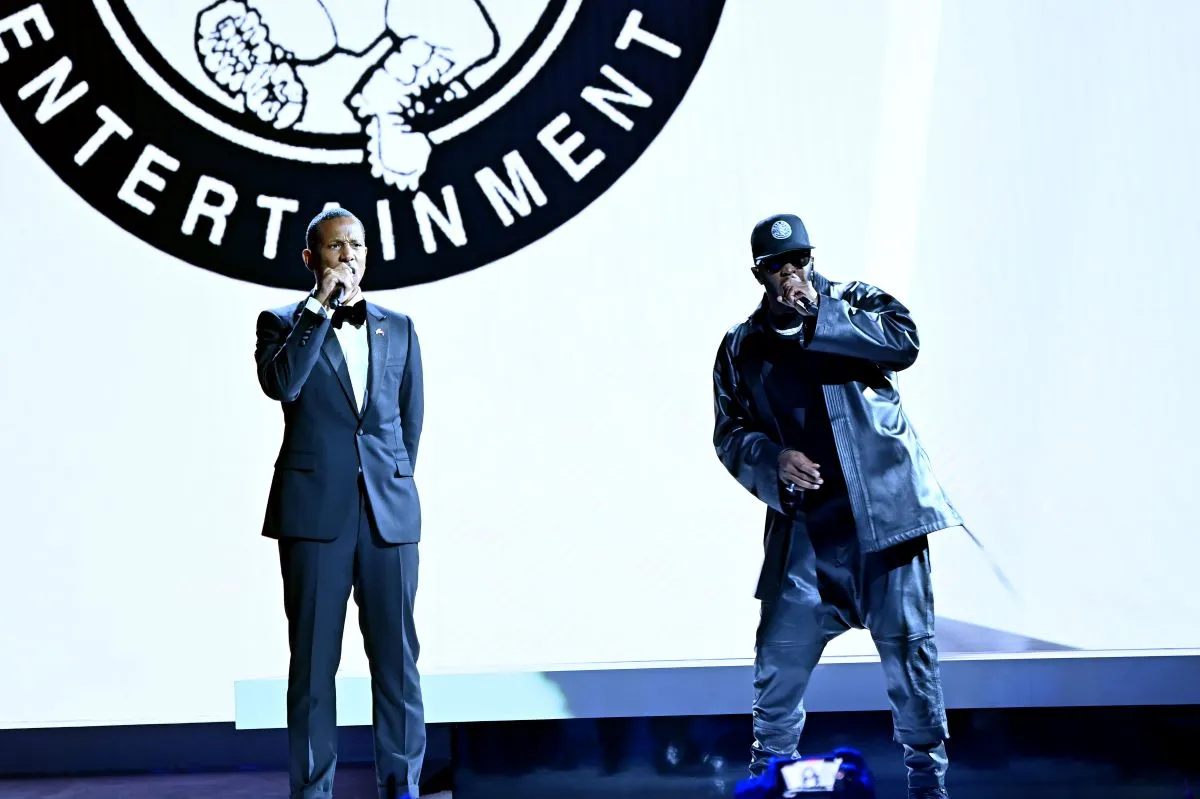 Shyne wears a suit and stands next to Sean 'Diddy' Combs on a stage.