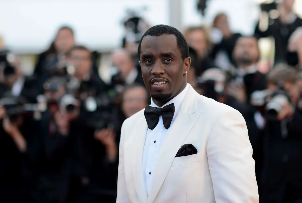 Sean 'Diddy' Combs wears a white tuxedo and stands in front of photographers.