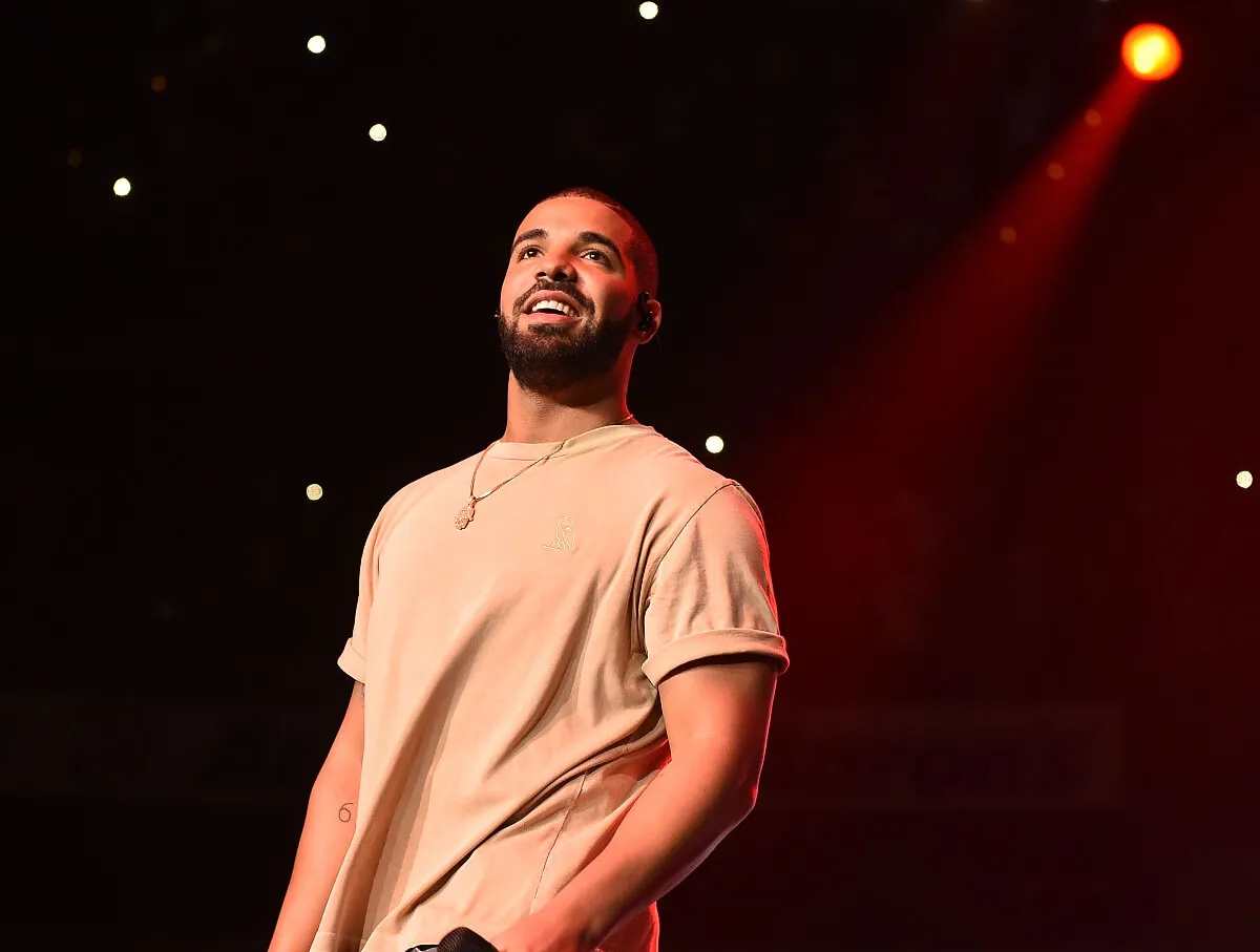 Drake wears a white shirt and stands on a stage.