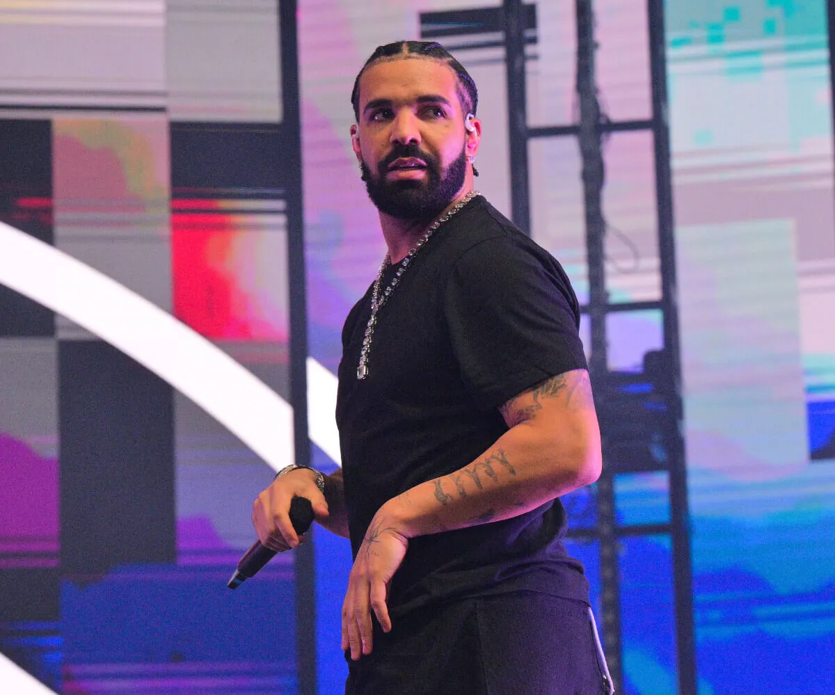 Drake wears a black shirt and holds a microphone.