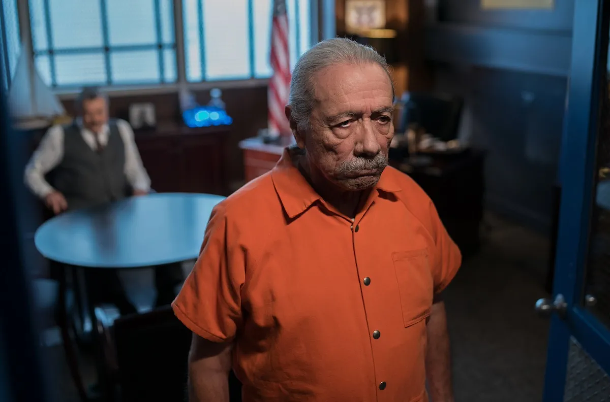 Edward James Olmos, standing in the foreground in an orange prison jumpsuit with Tom Selleck sitting at a desk behind him in the 'Blue Bloods' series finale